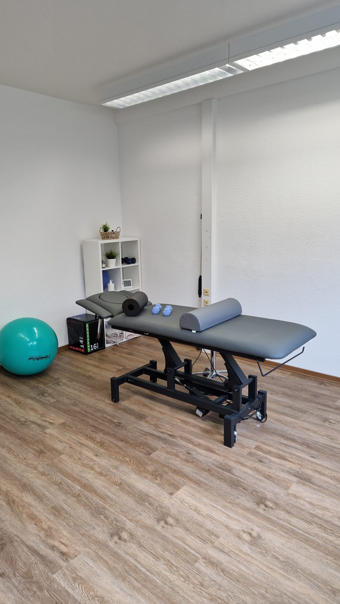 Therapieliege mit Faszienrolle, Kissen und Hanteln im Behandlungsraum.