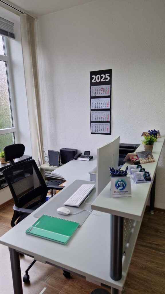 Empfangsbereich der Praxis mit Schreibtisch, Kalender und Büroausstattung.