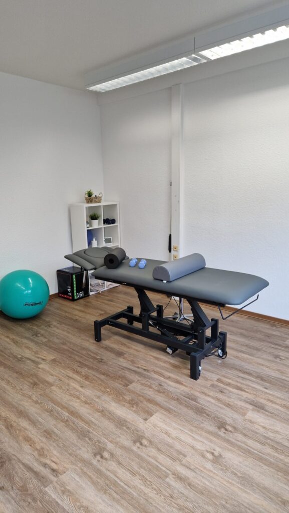 Trainingsgeräte und Liege für individuelle Therapie Therapieliege mit Faszienrolle, Kissen und Hanteln im Behandlungsraum.