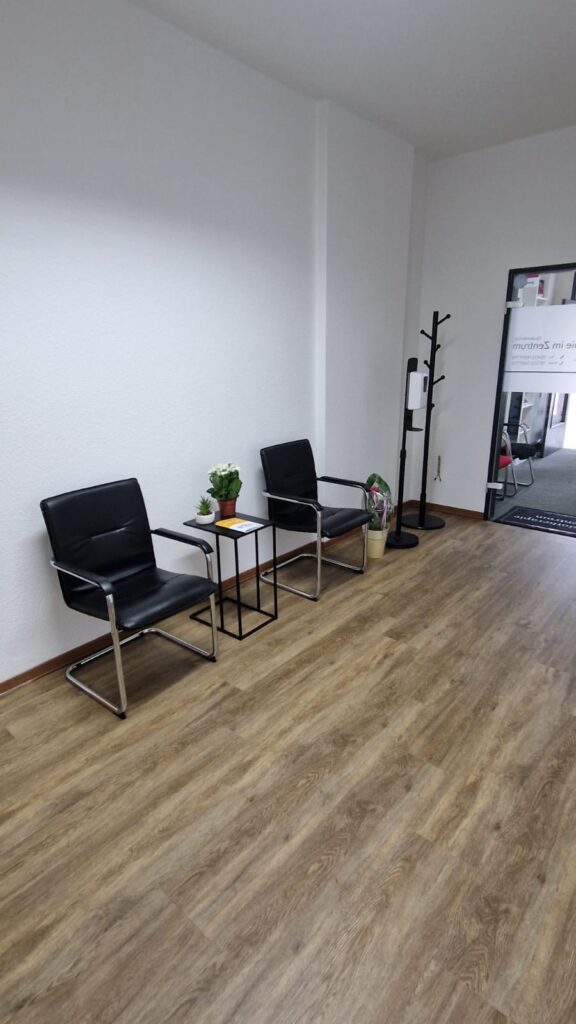 Modernes Wartezimmer mit schwarzen Sesseln, Pflanzen und Desinfektionsspender.